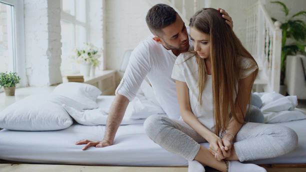 Couple sitting on a bed, man whispers to woman