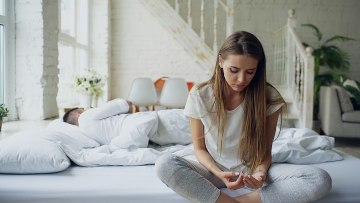 Woman sitting on bed, man sleeping behind her