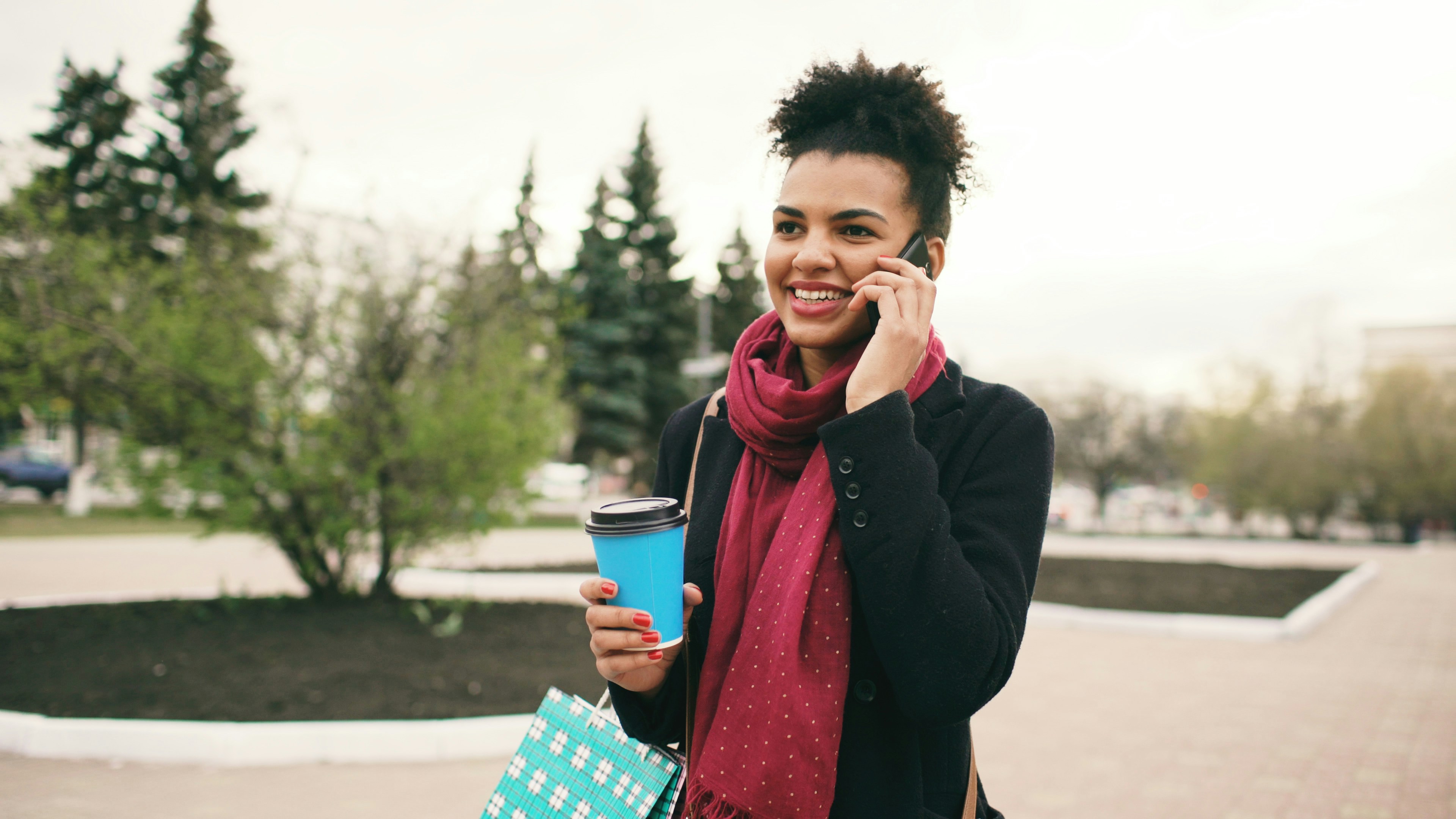 Woman holding coffee cup and talking on phone outdoors.