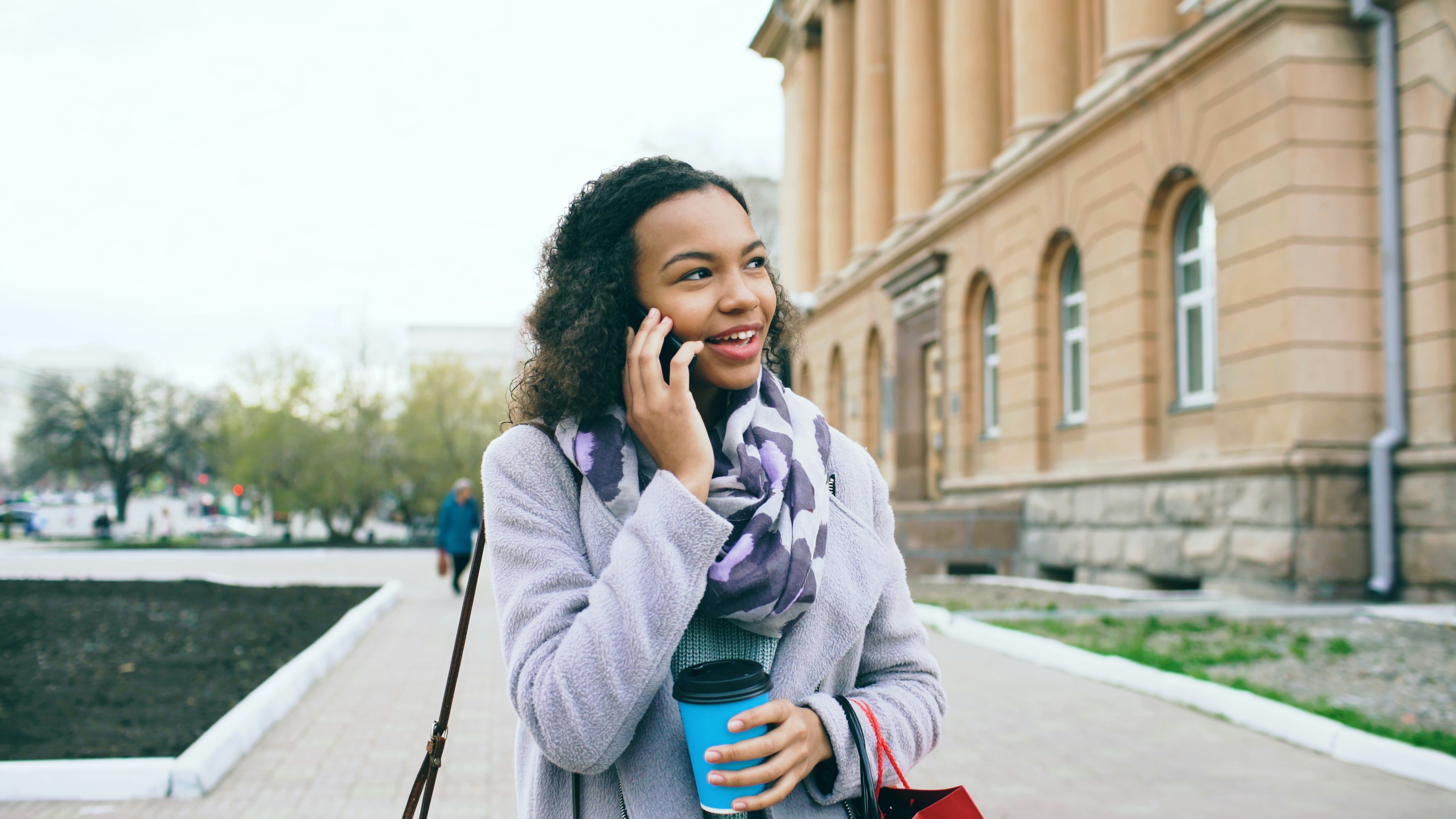 A woman talking on the phone and holding coffee.