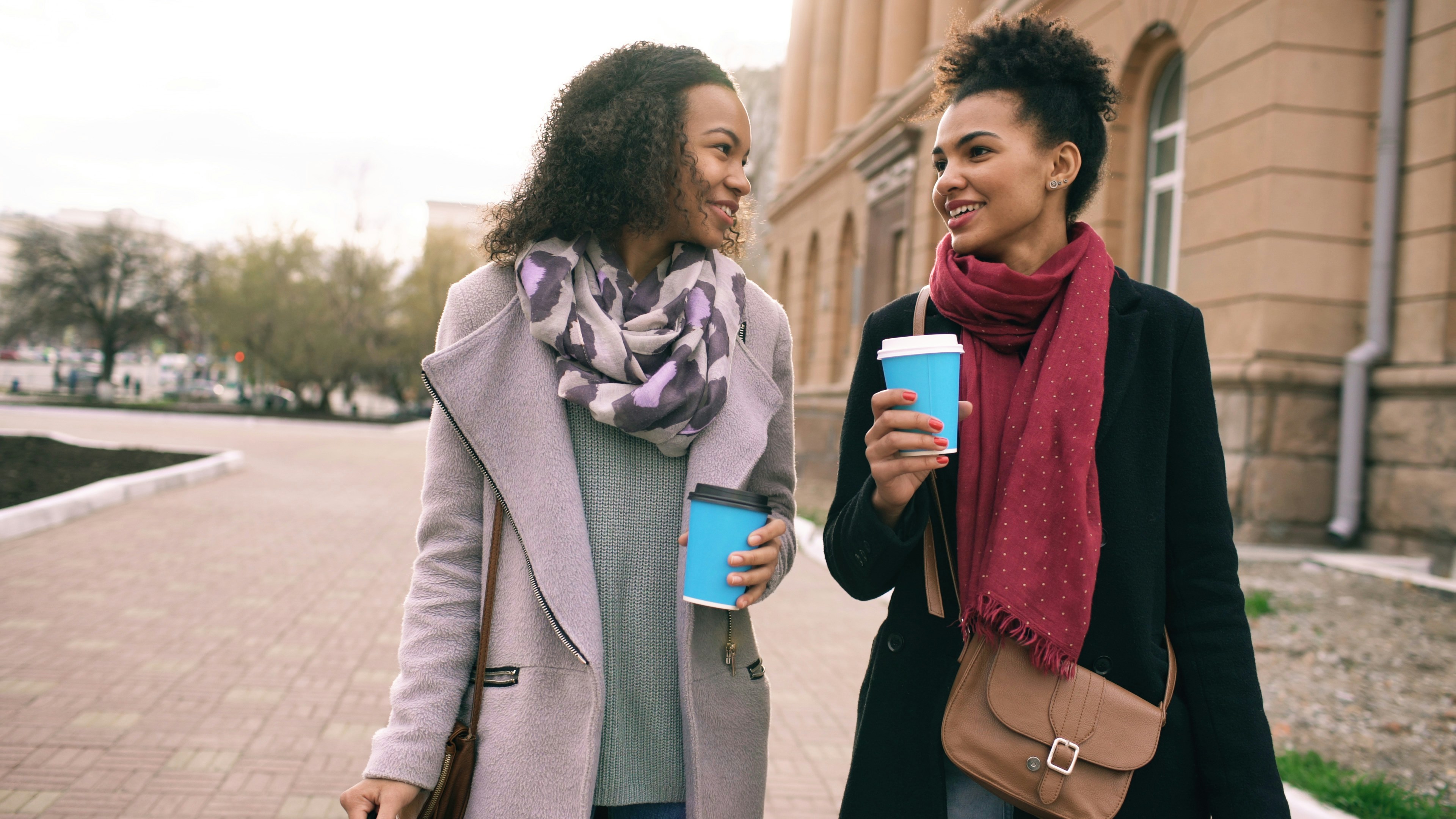 Two beautiful mixed race woman friends drink coffee and talking after shopping and walking city street