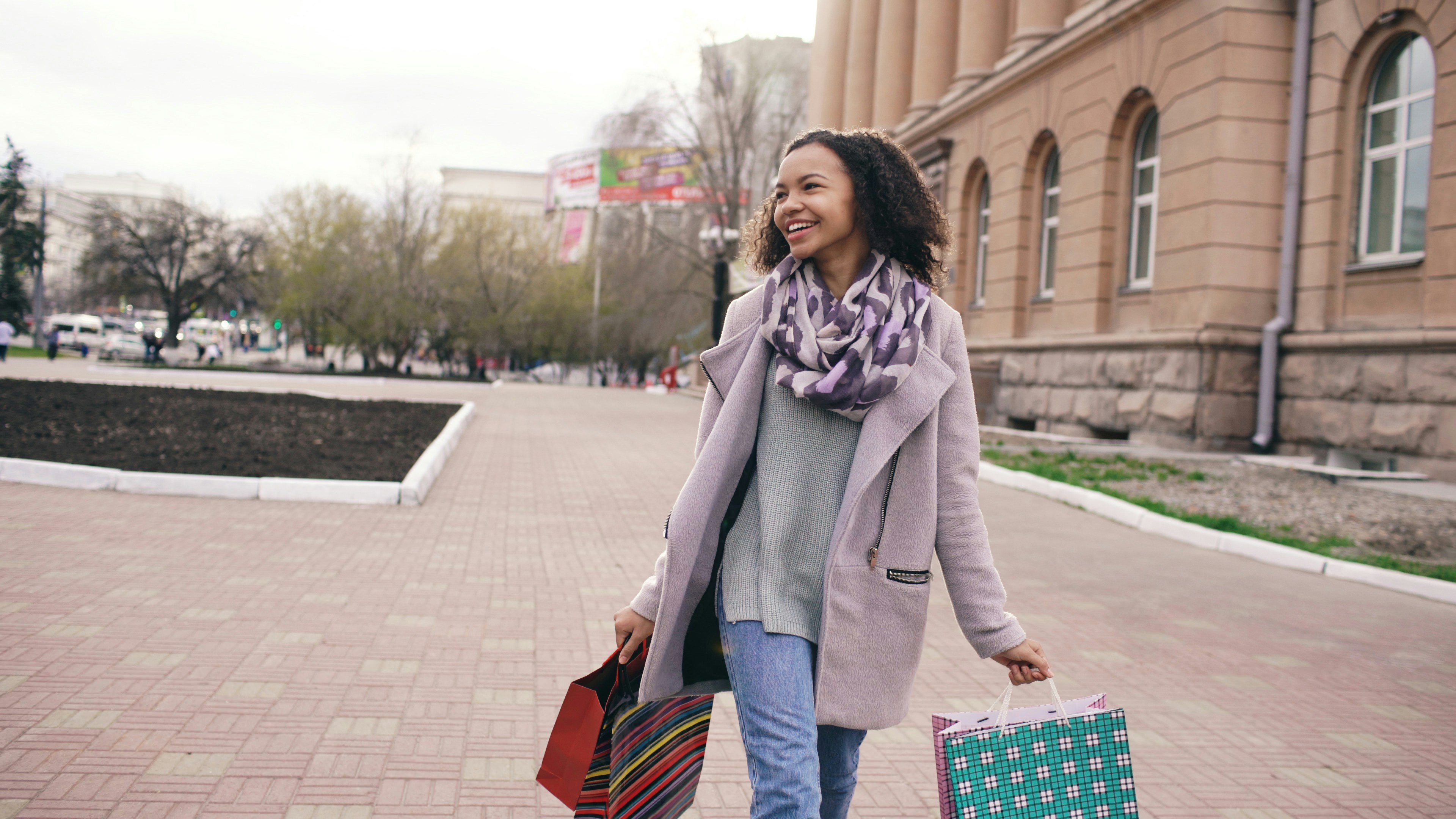 A smiling woman walks with shopping bags.