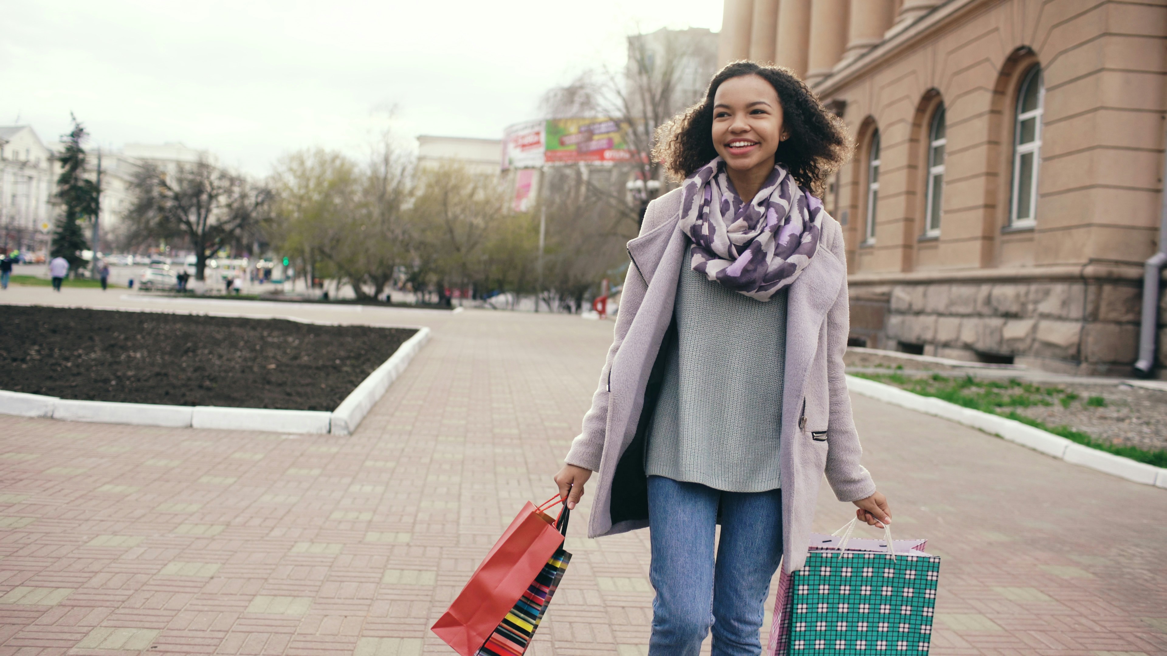 A smiling woman walks with shopping bags.
