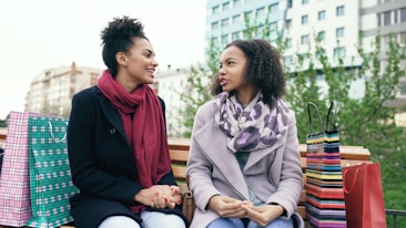 Two women sitting on a bench with shopping bags.