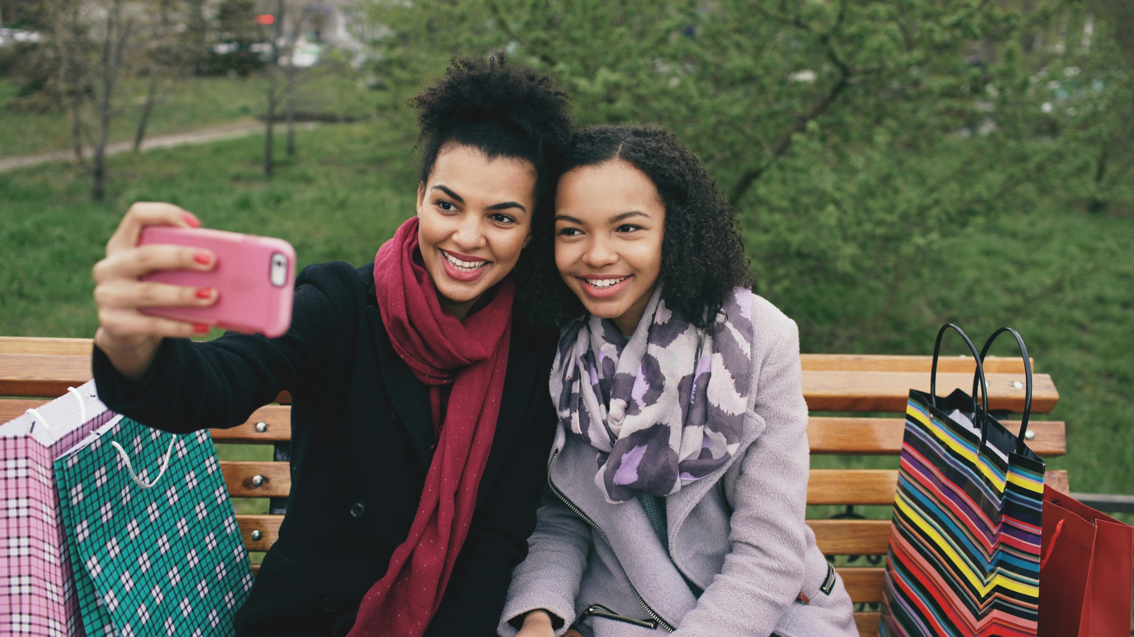 Two smiling women take a selfie on a bench.