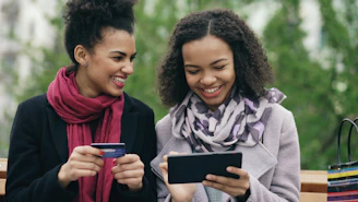 Two smiling women looking at a tablet with credit card.