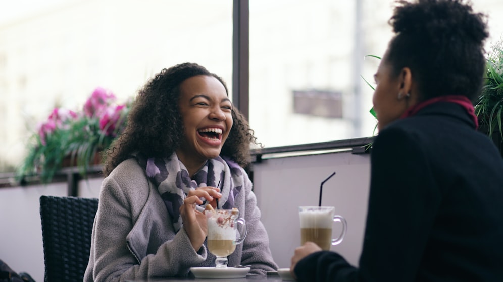 Duas amigas rindo e conversando descontraidamente em um cafe