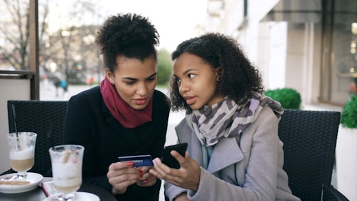 Two women smiling while shopping on a phone with a credit card