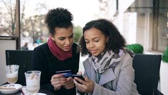 Two women looking at a smartphone with credit card