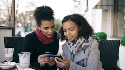 Two women looking at a smartphone with credit card