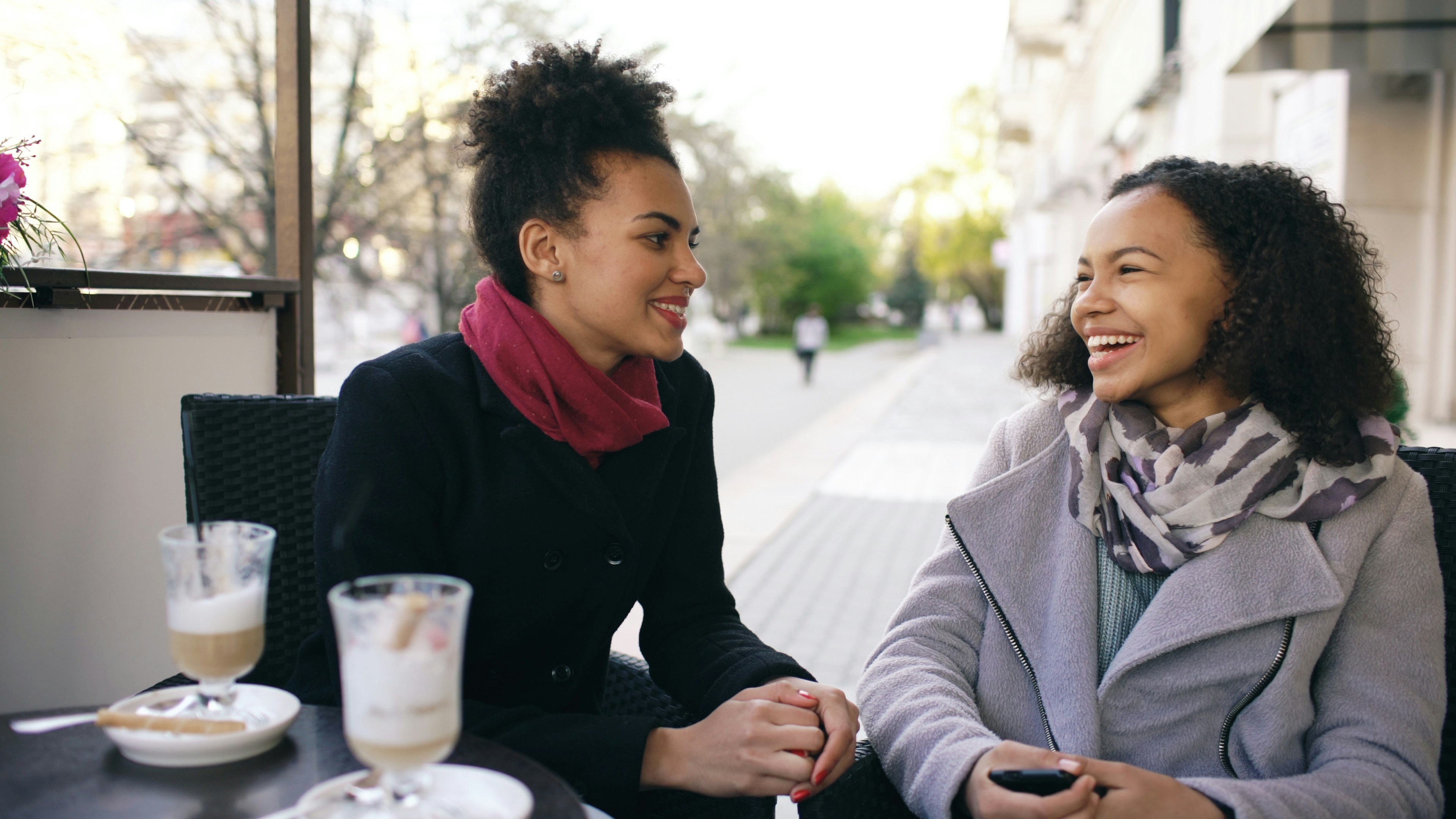 Two women laughing and talking at an outdoor cafe.