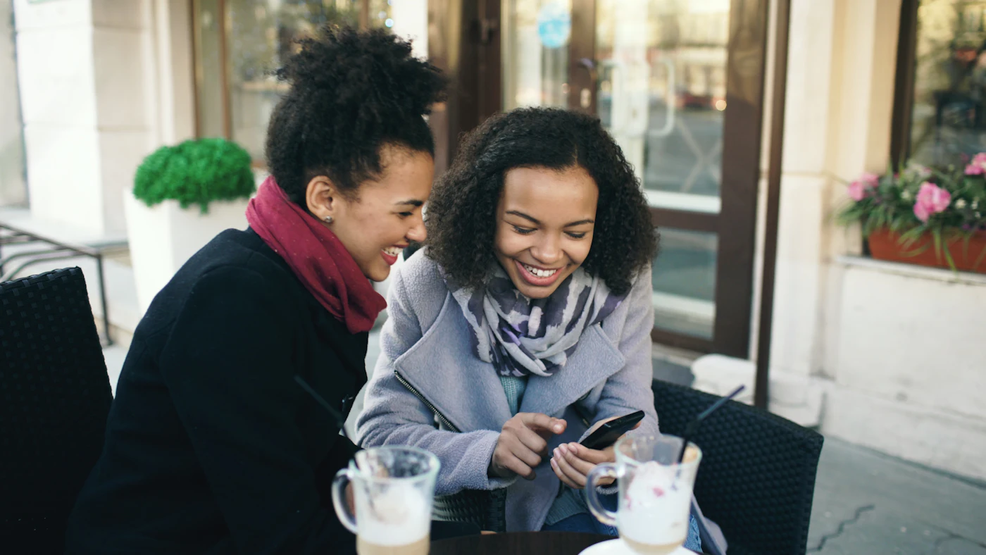 Dos mujeres riendo mientras miran un teléfono móvil en una terraza