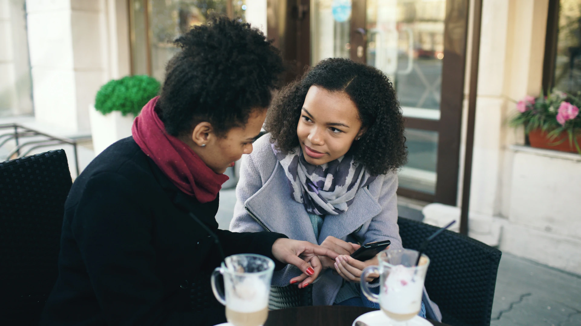 Two women talking at an outdoor cafe table.