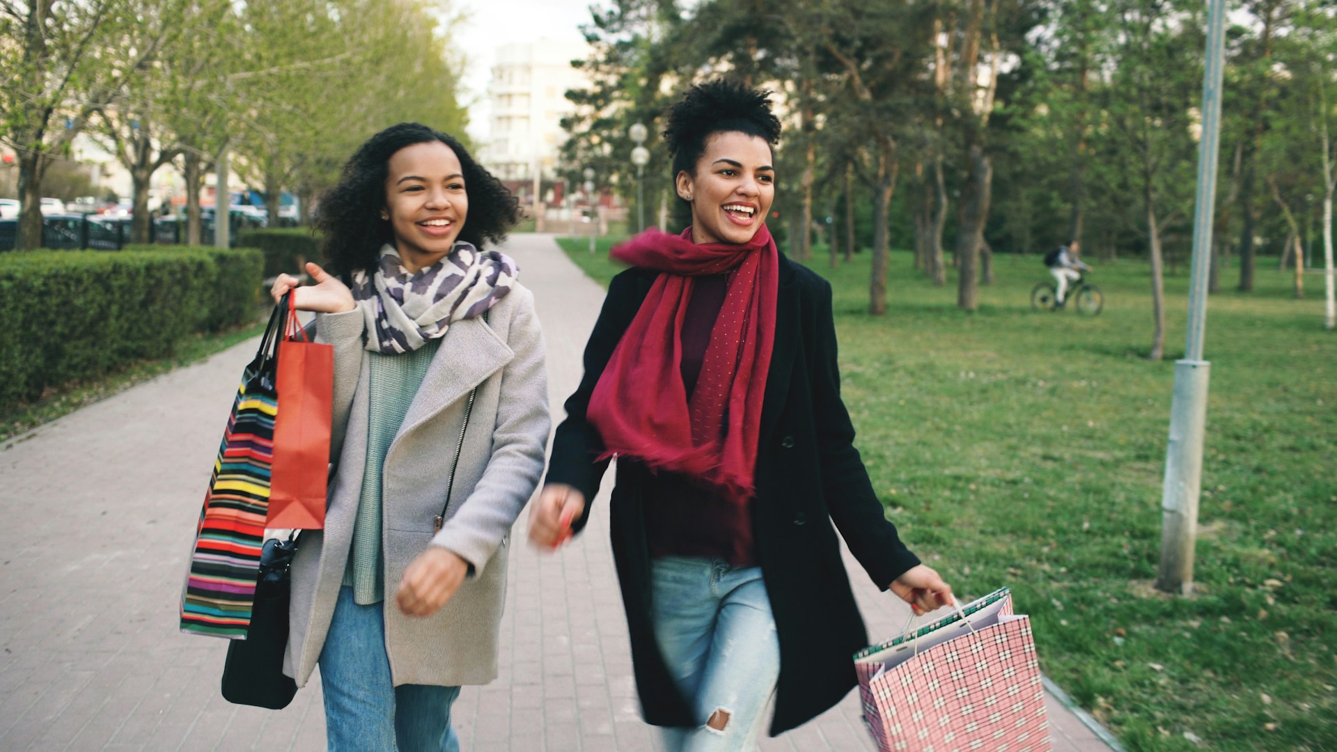 Two women walking with shopping bags in a park.