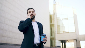 Man in suit talking on phone with coffee cup.