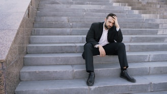Man in suit sitting on outdoor stairs looking down.
