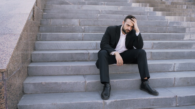 Man in suit sitting on outdoor stairs looking down.