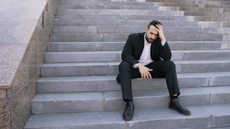 Man in suit sitting on steps, head in hand.