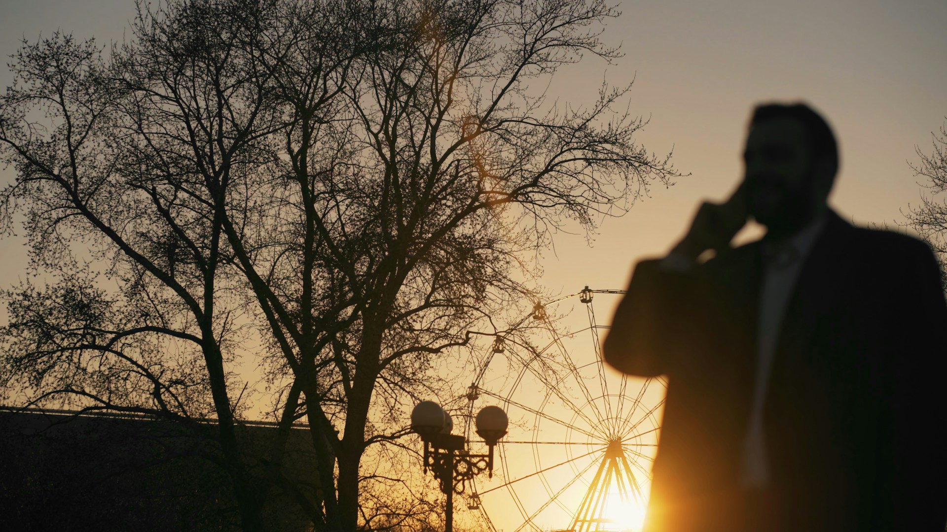 Man on phone with ferris wheel at sunset
