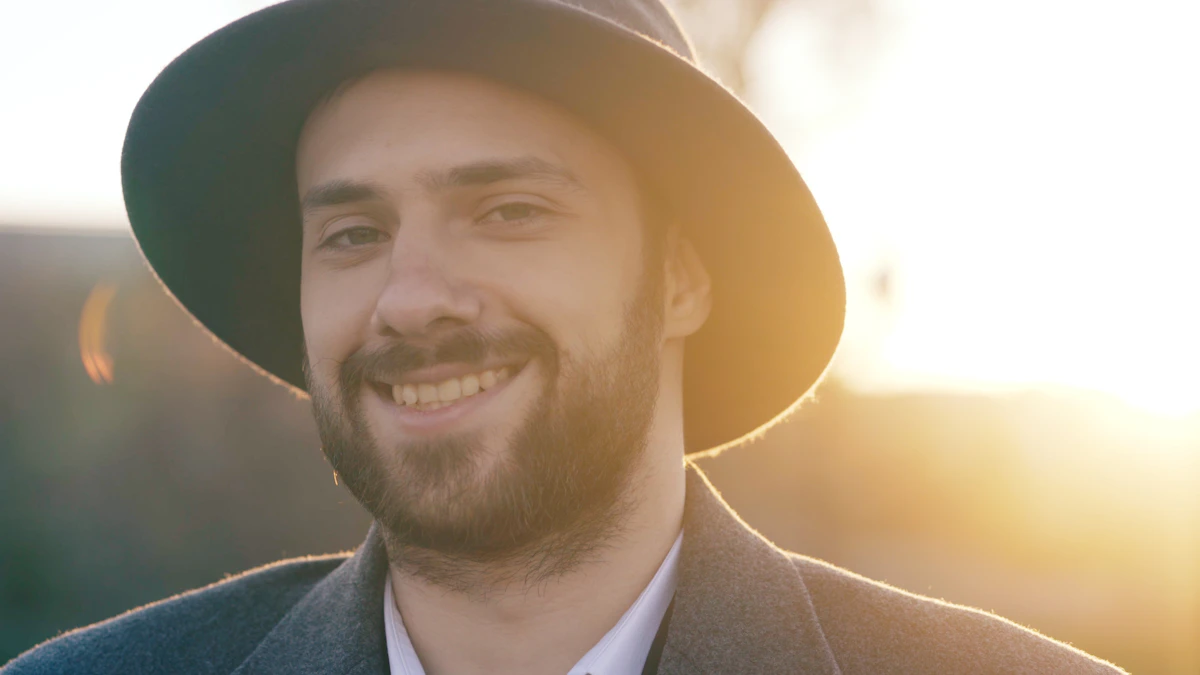 A man in a hat smiling outdoors at golden hour, calm and doing well