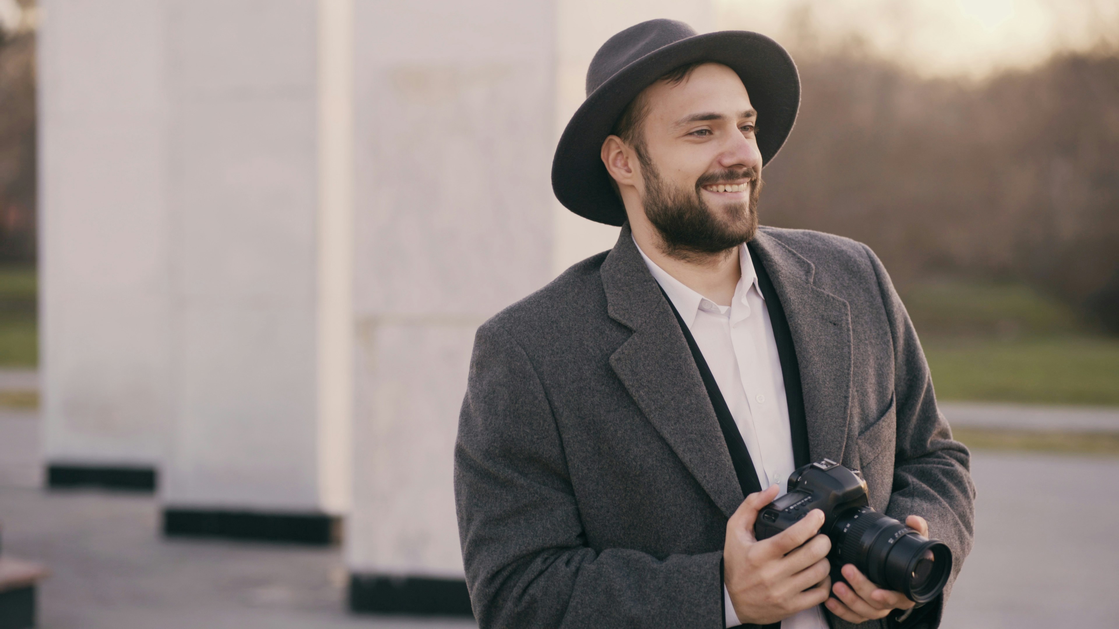 Stylish young photographer man in hat standing outdoors and photographing tourist sightseeing during travel