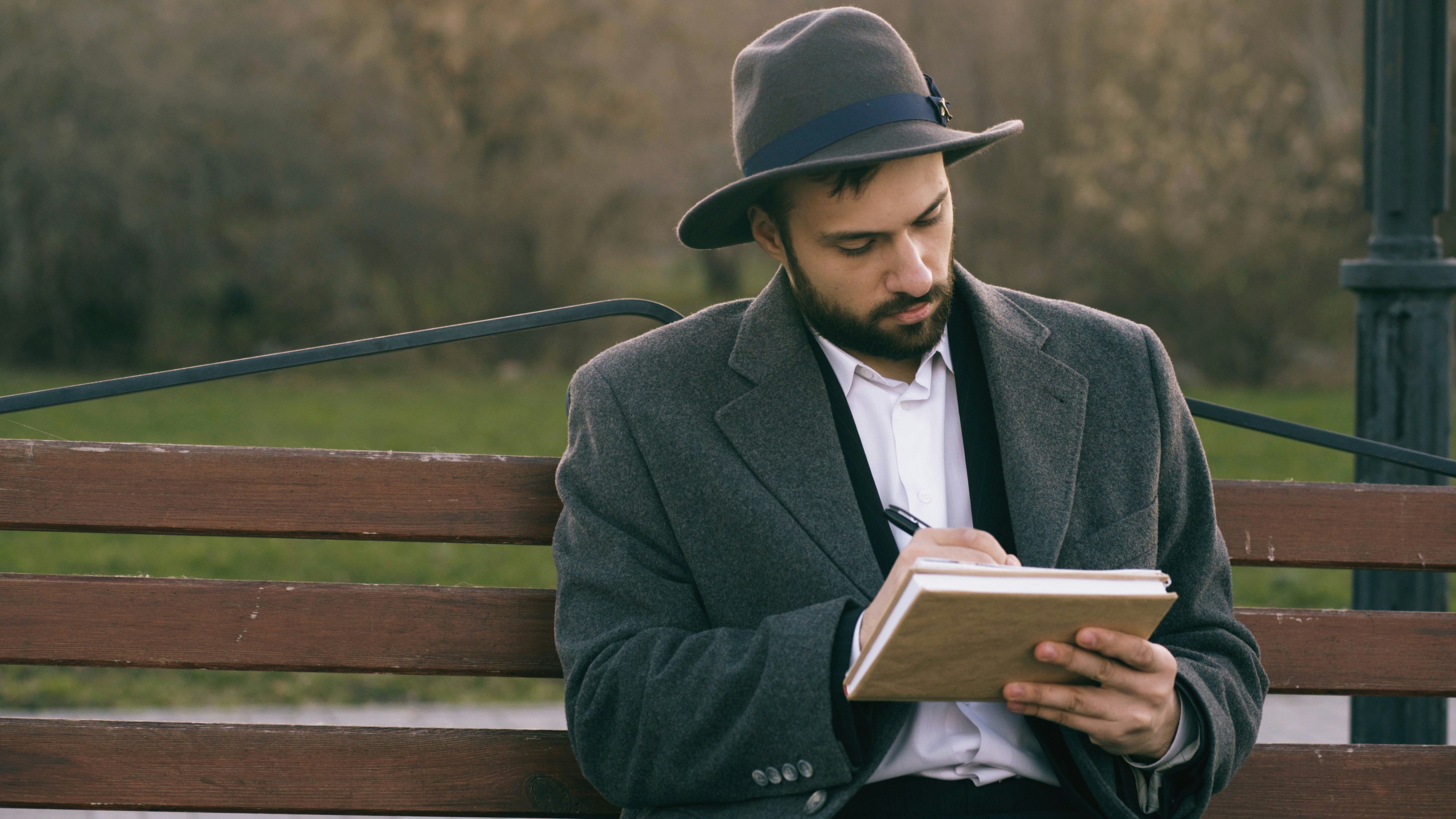 Man in hat writing in notebook on park bench