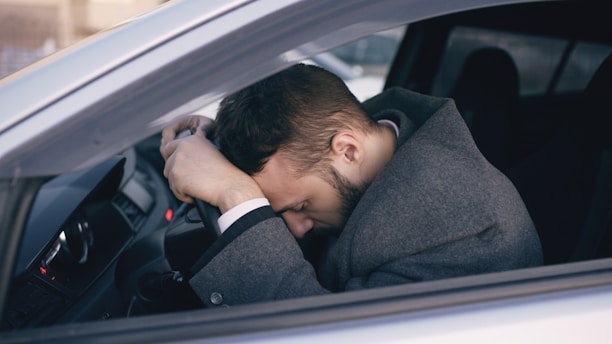 Man resting head on steering wheel in car.