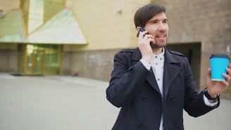 Man talking on phone holding blue coffee cup outside building