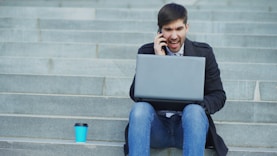 Man i telefonen som sitter i trapportna med en blå kopp brevid sig