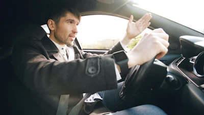 Man driving a car, gesturing with hand.