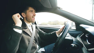 Man singing and driving a car enthusiastically.
