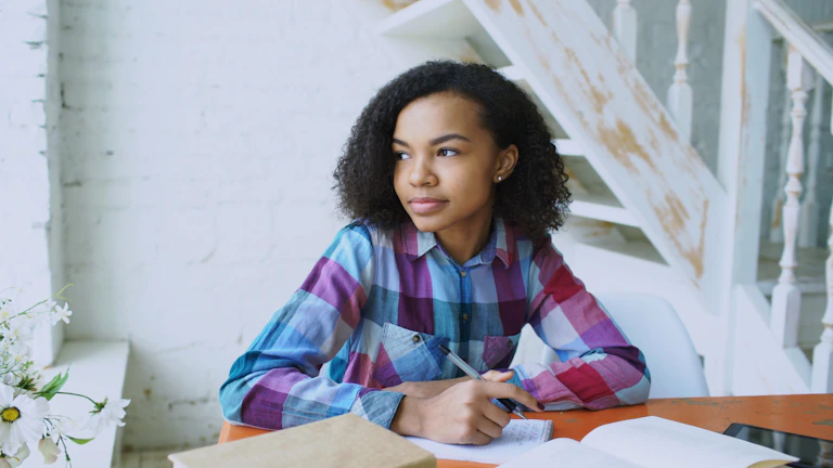 Young woman writing at a table with open book.