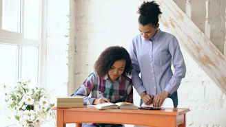 Woman helps girl with homework at desk.