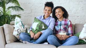 Two smiling young women watching television with popcorn.
