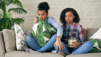 Two women watching TV with a pillow and popcorn