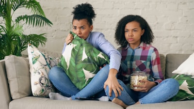 Two women watching TV with a pillow and popcorn