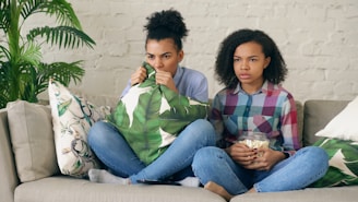 Two women sitting on a couch looking concerned.