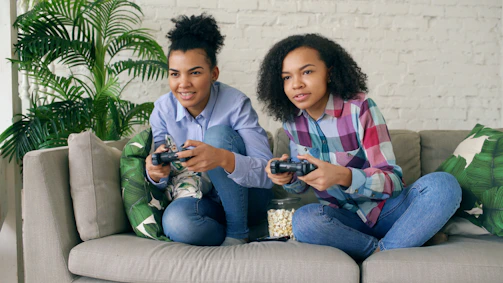 Two young women playing video games on a couch.