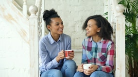 Two young women drinking coffee on stairs