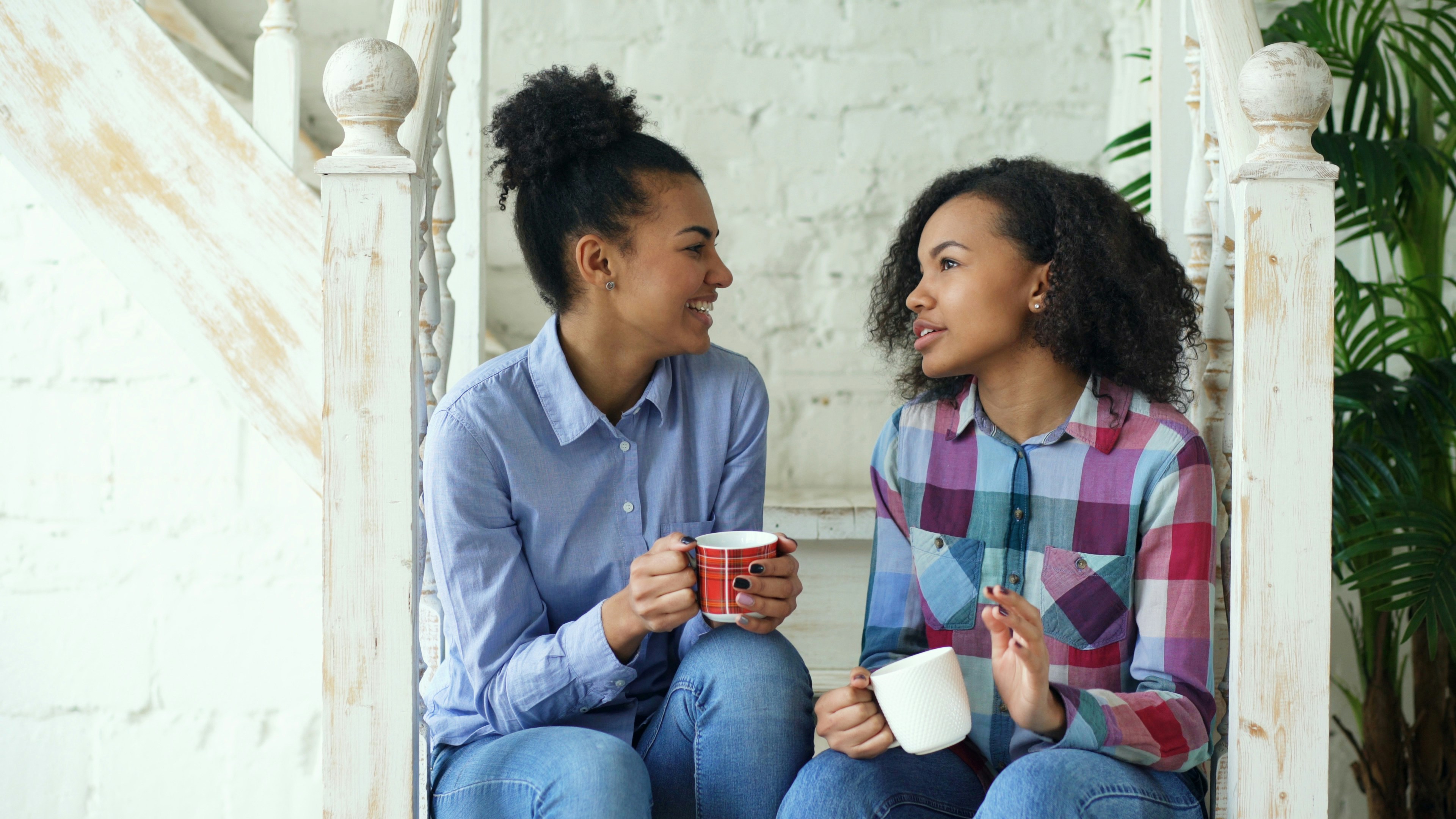Two women talking while holding coffee mugs on stairs.