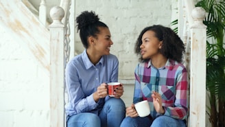Two women talking while holding coffee mugs on stairs.