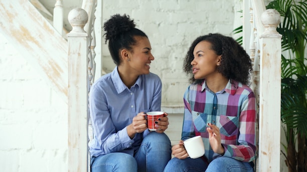 Two women talking while holding coffee mugs on stairs.