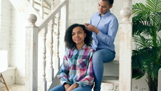Mother braiding daughter's hair on staircase.