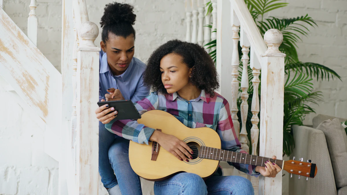 A young woman shows a teenage girl a chord on the guitar, a tablet open beside them