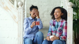 Two laughing women sitting on stairs with coffee cups