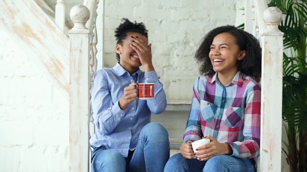 Two laughing women sitting on stairs with coffee cups