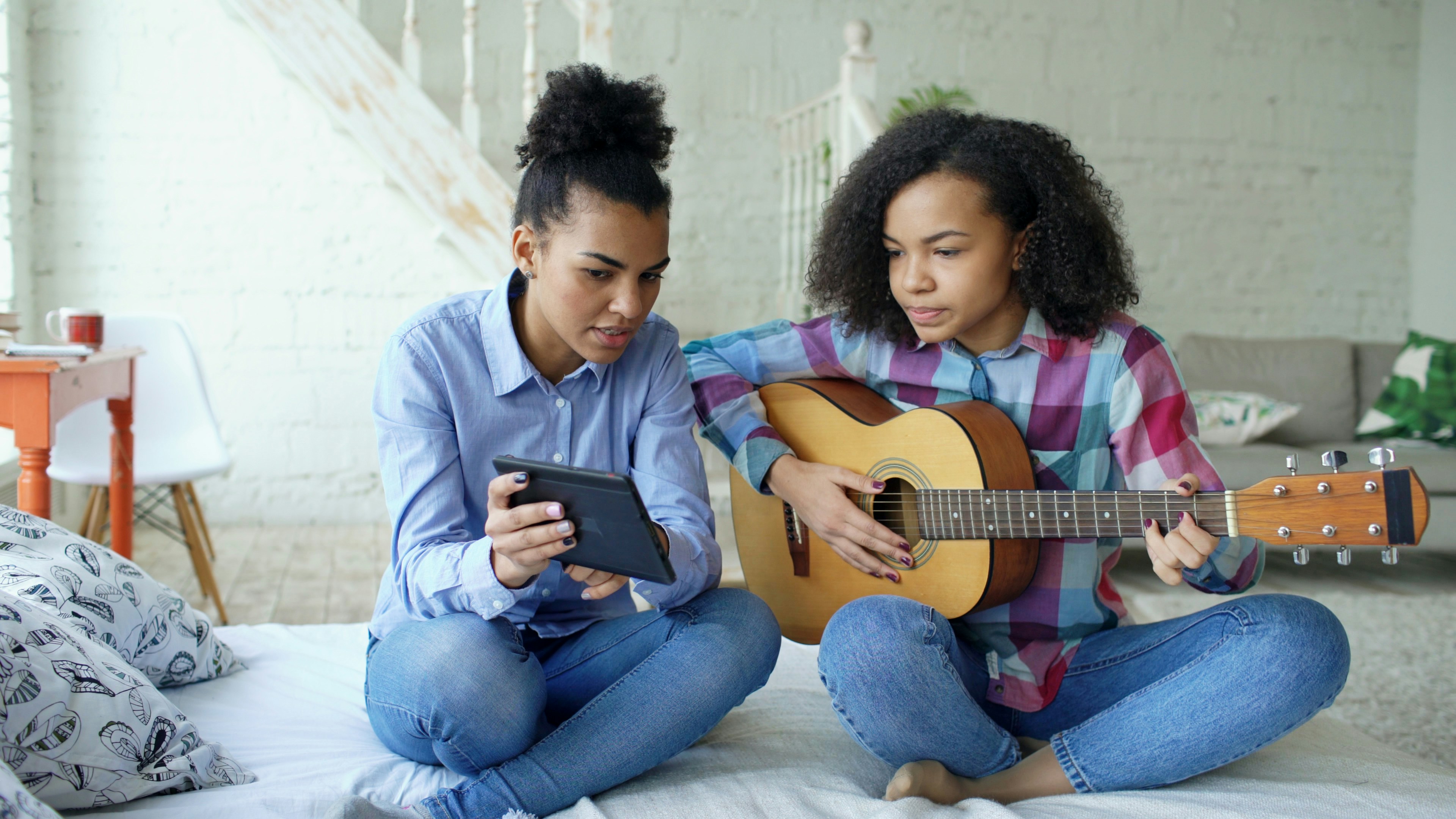 Two girls learning guitar from a tablet