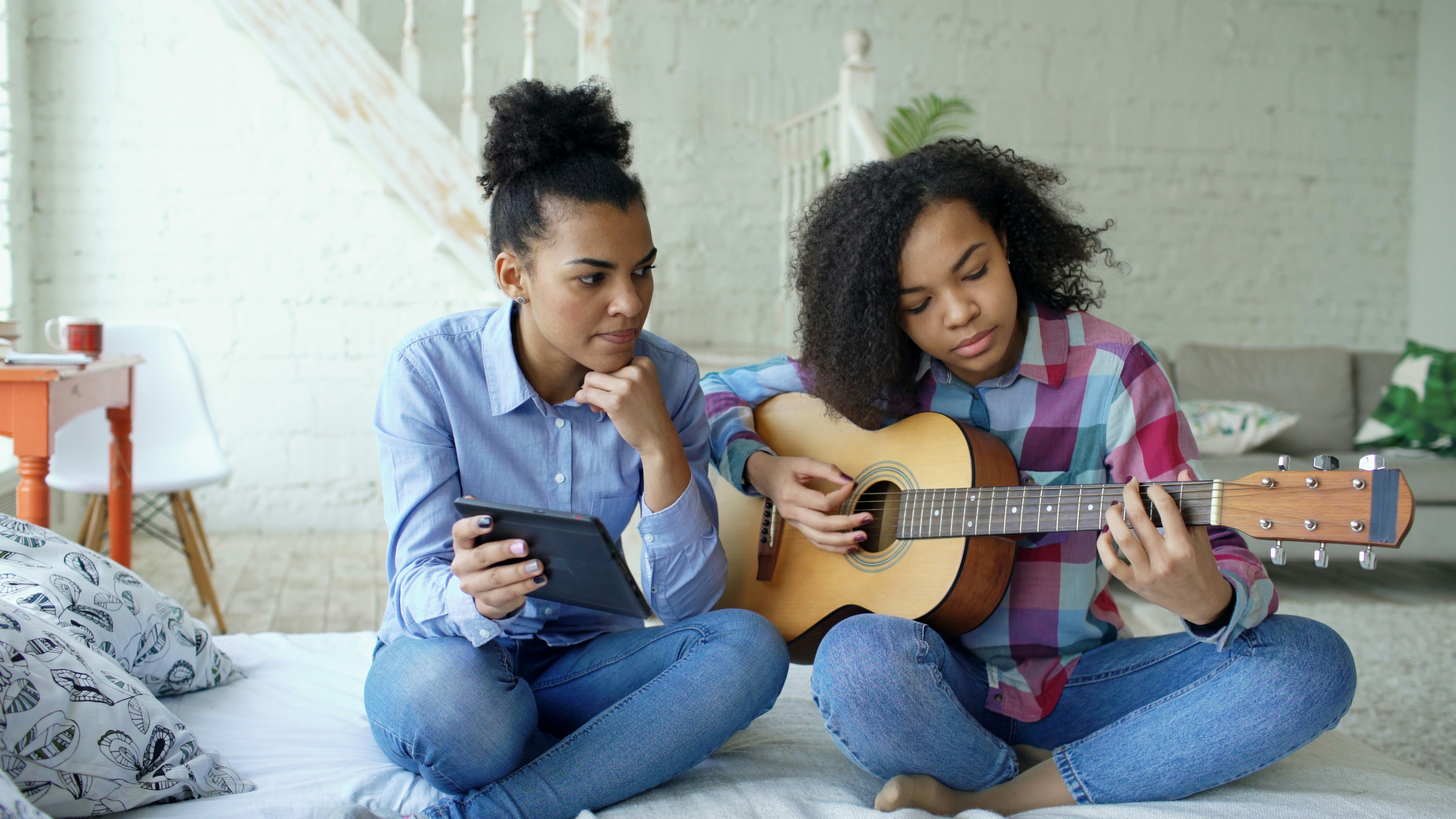 Two girls learning guitar together indoors.