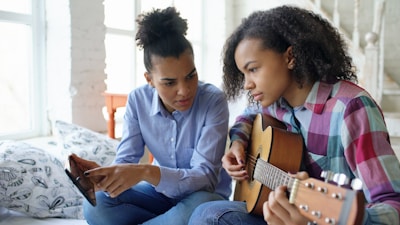 Two young women learning guitar together indoors.