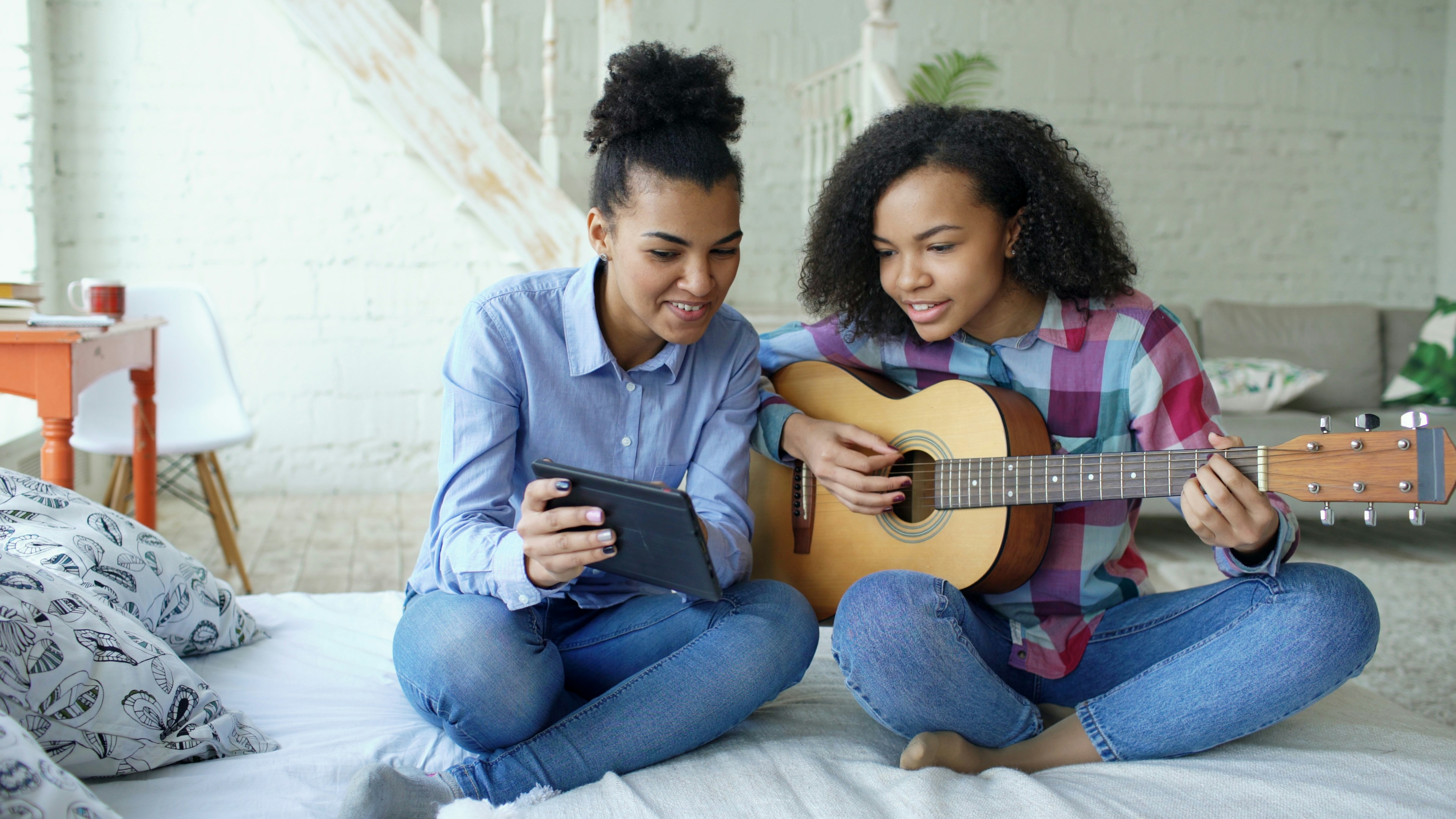 Two young women learning guitar from tablet